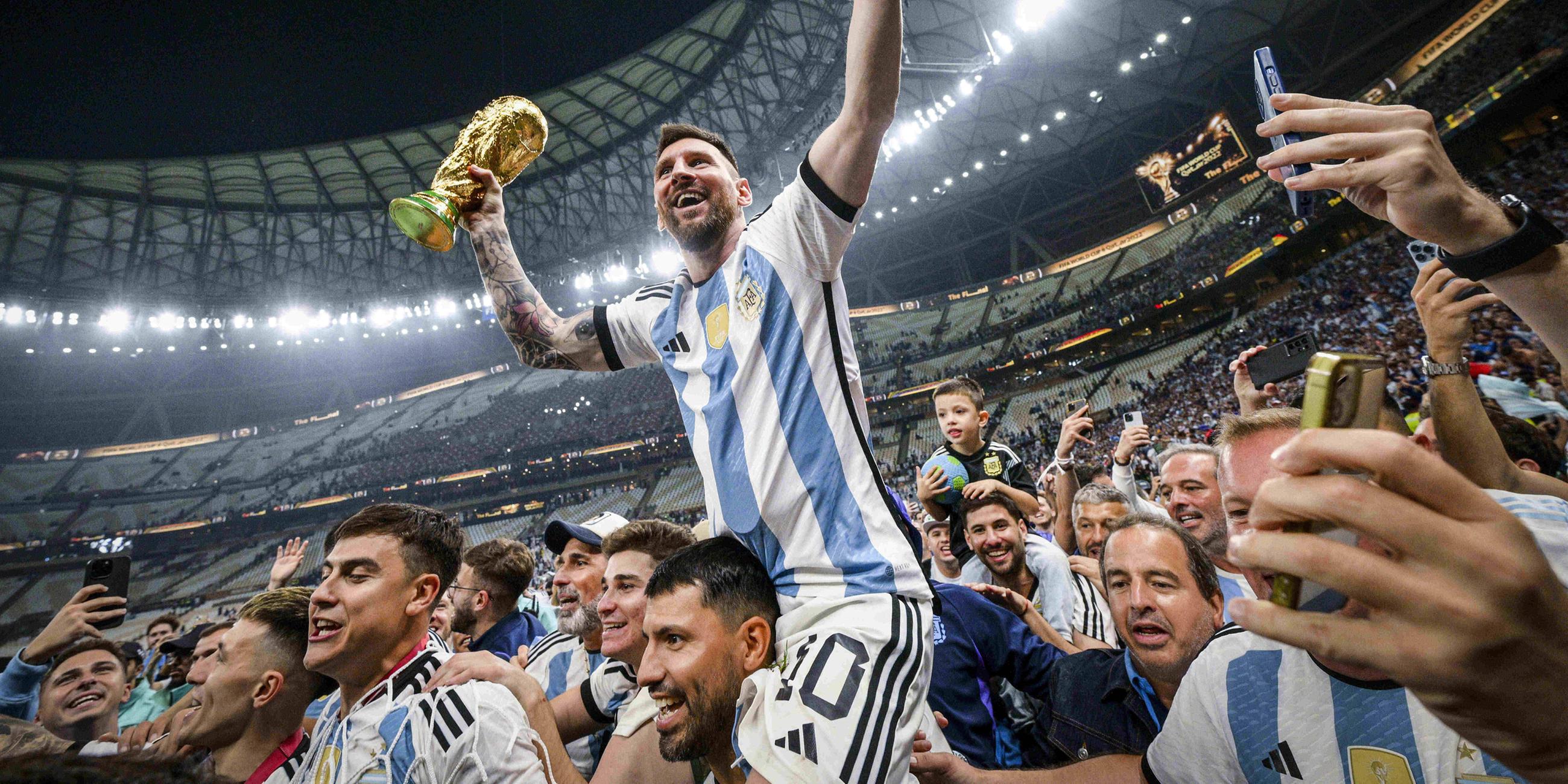 Lionel Messi hebt die WM-Trophäe hoch und wird von seinen Teamkollegen triumphierend getragen 