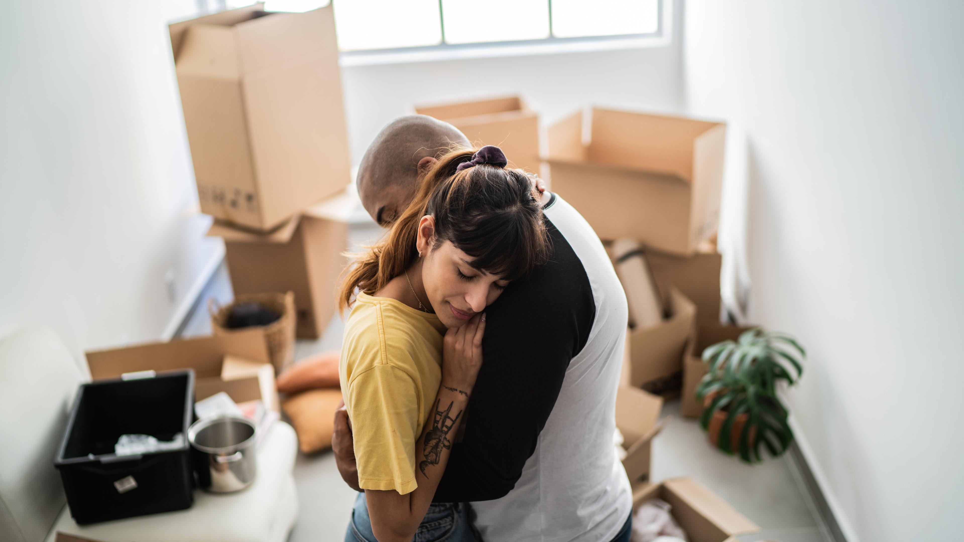Ein junges Paar umarmt sich vor Umzugskartons in einer Wohnung