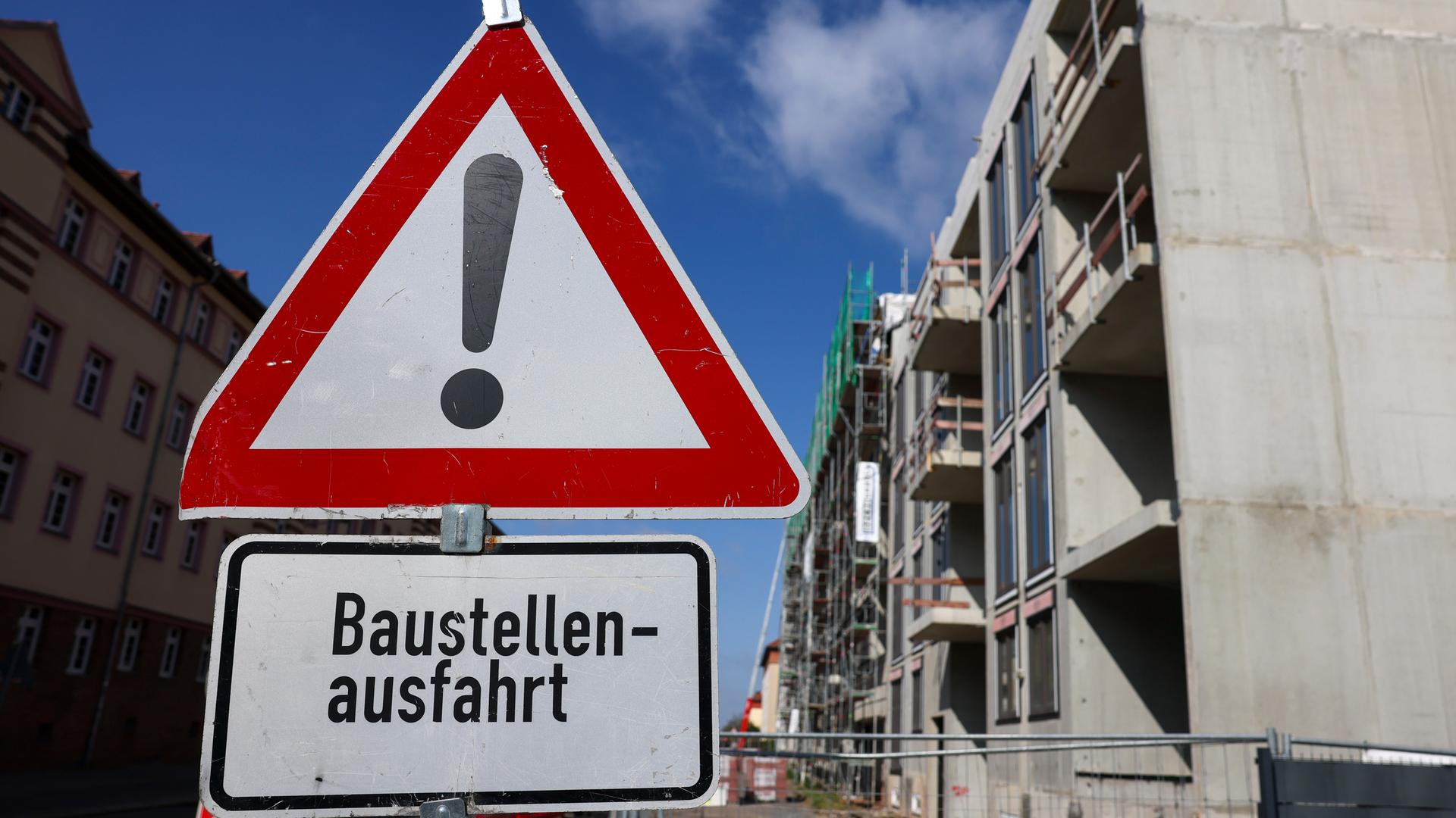 Typical für Wohnungsbau und Wohnraum: Rohbau im Hintergrund mit Warnschild und Schild "Baustellenausfahrt" im Vordergrund