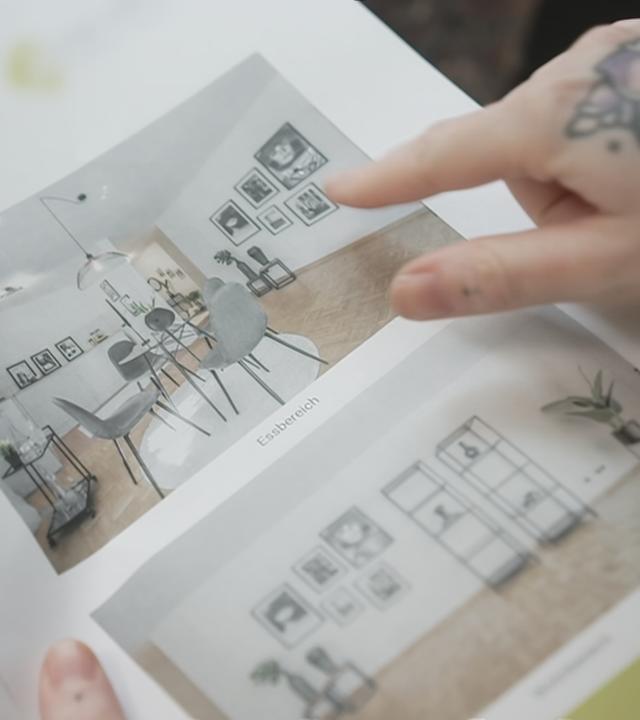 Eine Person zeigt mit dem Finger auf Bilder einer Wohnung.