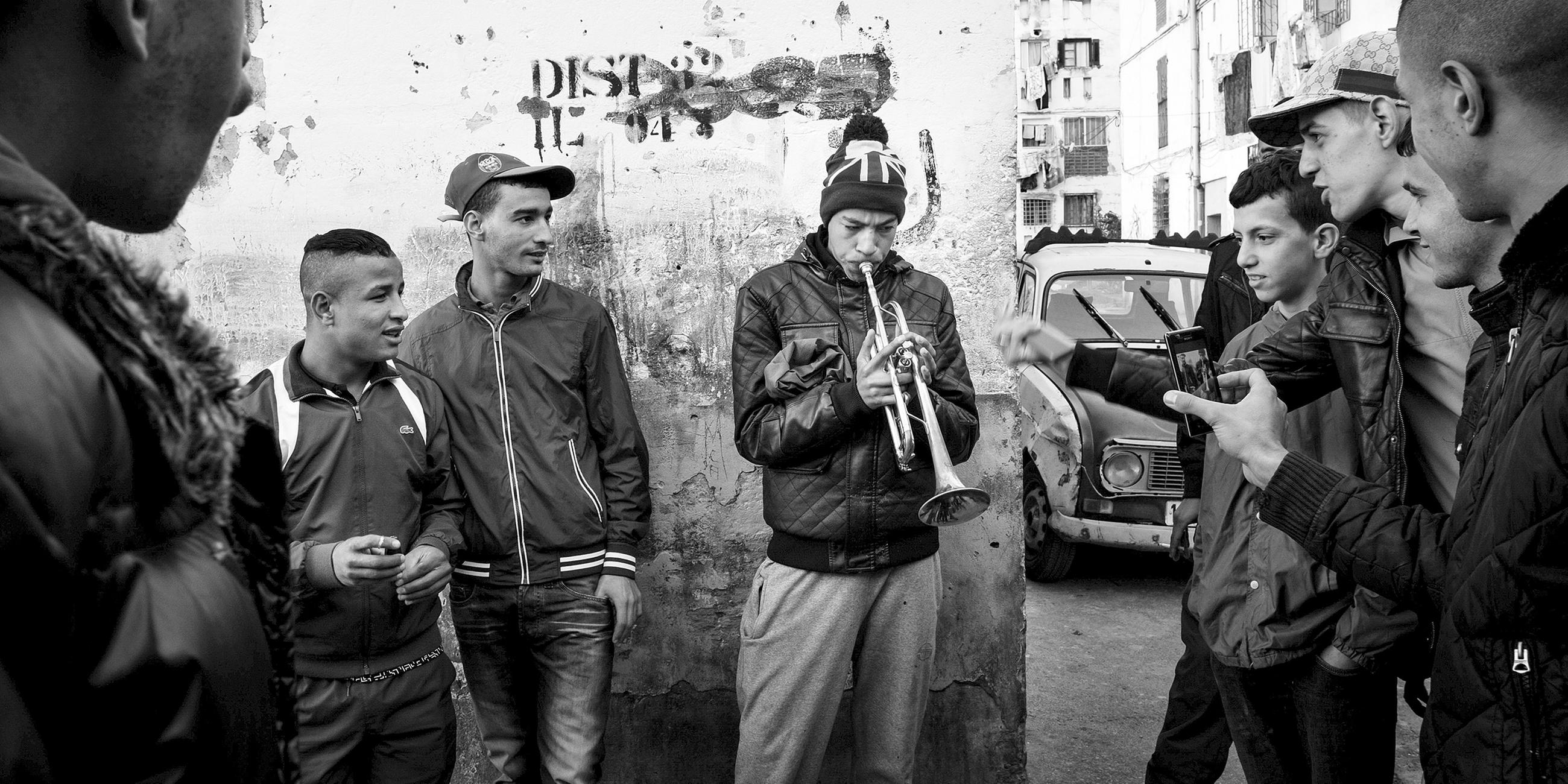 Algerien, Alger: Ein junger Mann hat Publikum, während er im überfüllten Viertel "climat de france" mit einer Trompete experimentiert.
