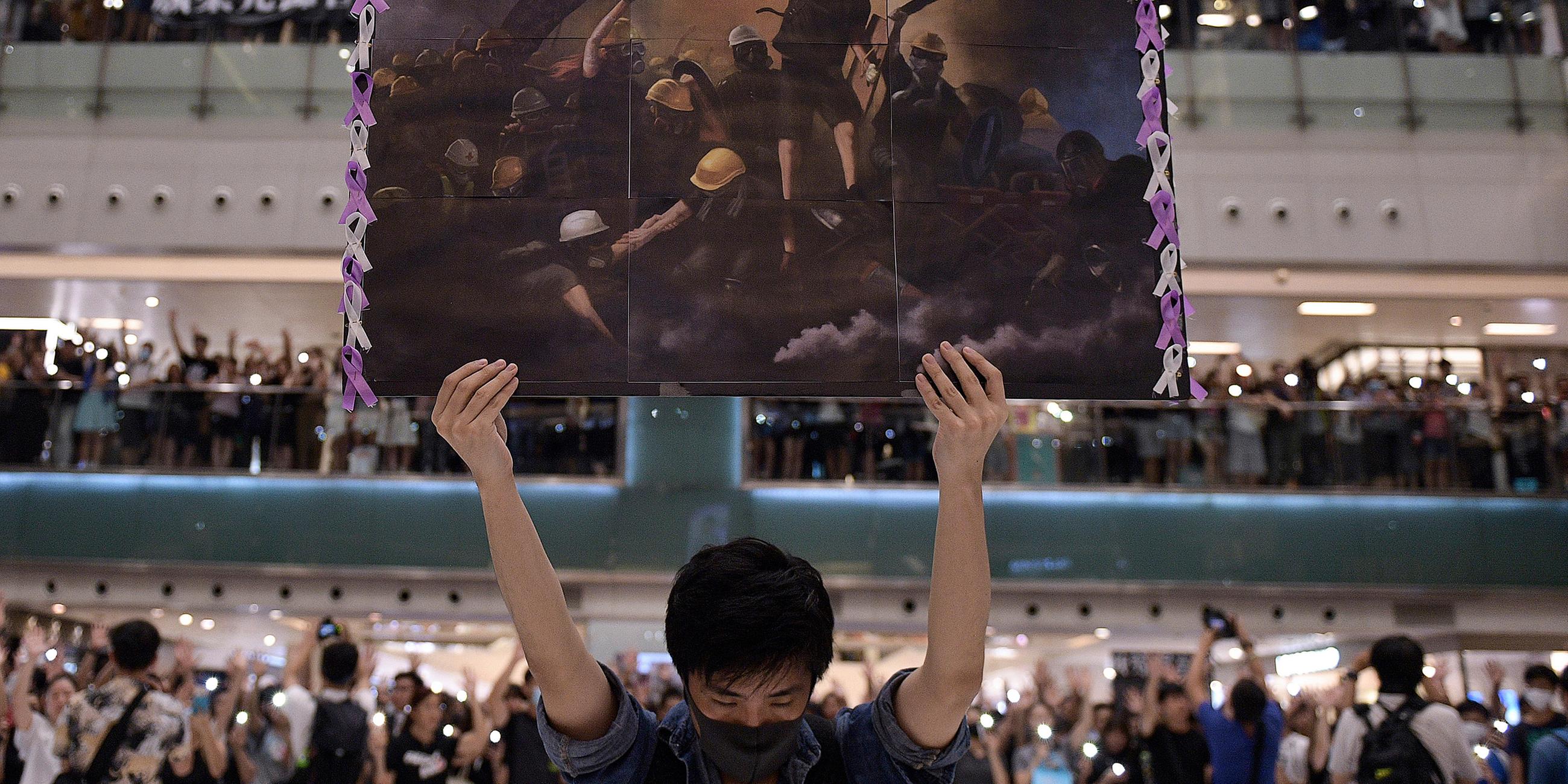Hongkong, Shatin: Ein Mann hält ein Plakat in der Hand, während sich die Menschen zum singen von 'Glory to Hong Kong' versammelt haben.