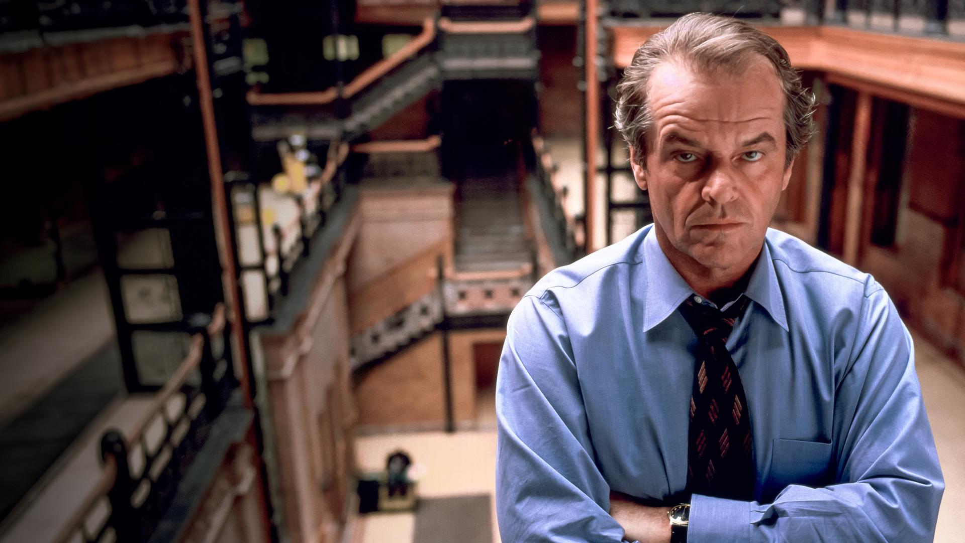 Großaufnahme von Will Randall (Jack Nicholson) der mit verschränkten Armen in einer Art Bibliothek steht und ernst nach vorne blickt.