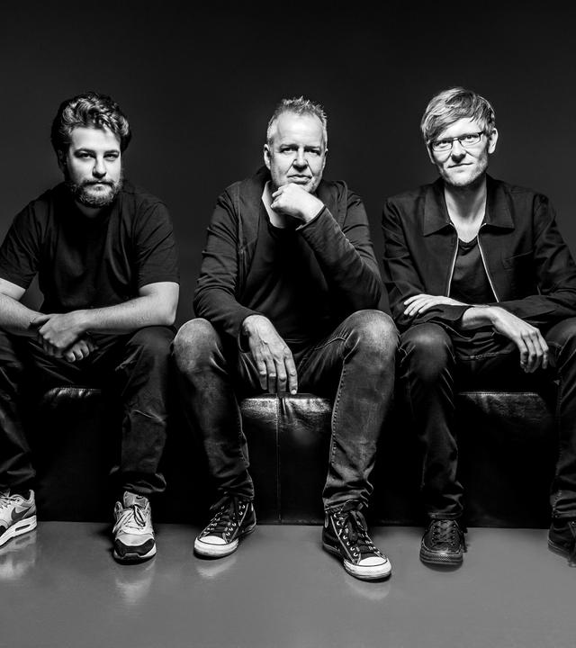 Wolfgang Haffner und Mitmusiker sitzen auf einer Stufe und schauen in die Kamera, schwarzweisses Bild, legere Kleidung und Turnschuhe, trotzdem elegant.