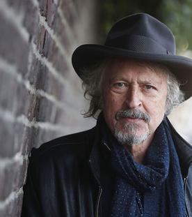 Mann mit Hut steht an einer Mauer und schaut in die Kamera