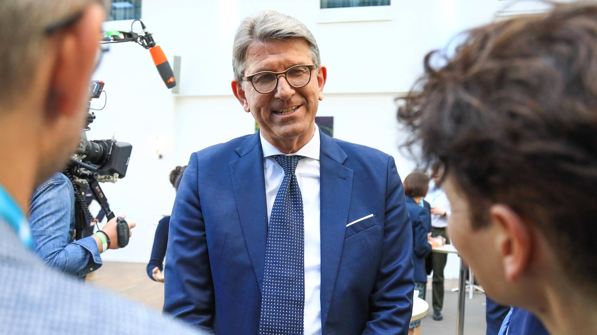 Ein älterer Mann mit Brille und im Anzug wird interviewt.