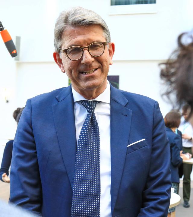 Ein älterer Mann mit Brille und im Anzug wird interviewt.