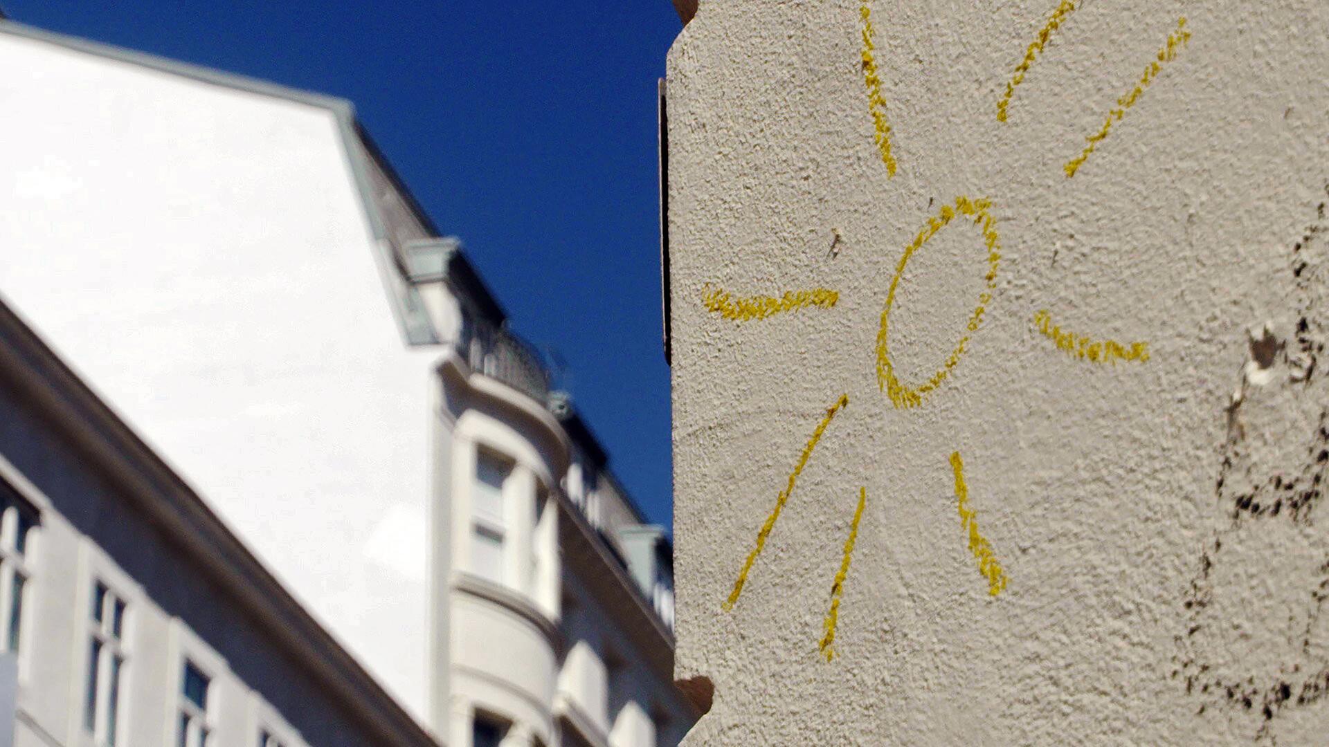 Eine gemalte gelbe Sonne auf einer hellen Hauswand.