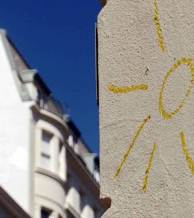 Eine gemalte gelbe Sonne auf einer hellen Hauswand.