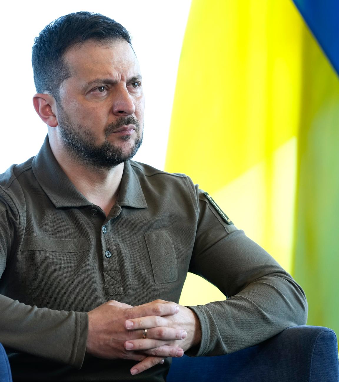 Wolodymyr Selenskyj sitzt auf einem Stuhl vor der ukrainischen Flagge
