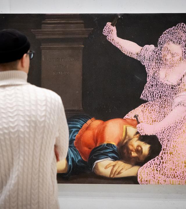 Ein Paar schaut sich ein großformatiges Bild an, auf dem ein Mann in historischer Kleidung schlafend auf dem Boden liegt, während eine Frau, die nur als verwitterter Umriss zu sehen ist, über ihm kniet und mit einer Hand ausholt.