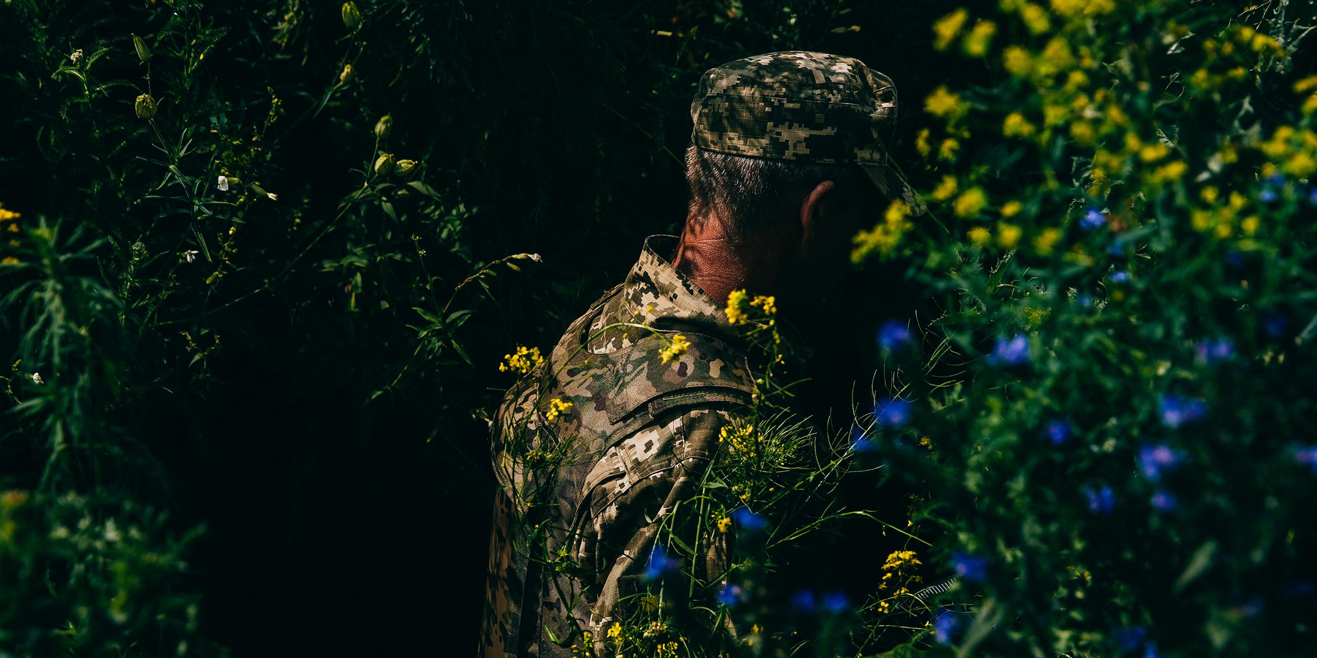 Ein ukrainischer Soldat steht in einem Gebüsch mit blühenden Sträuchern.