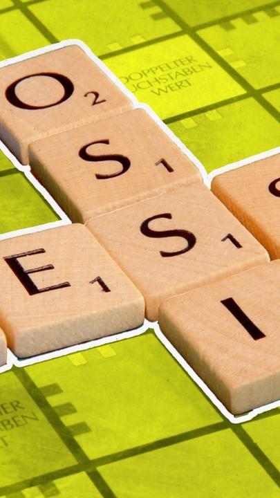 Ein Scrabble-Brett mit den Worten „Ossi” und „Wessi”, die sich in der Mitte überschneiden. Das Wort Ossi gibt 5 Punkte und das Wort Wessi ergibt 7 Punkte.
