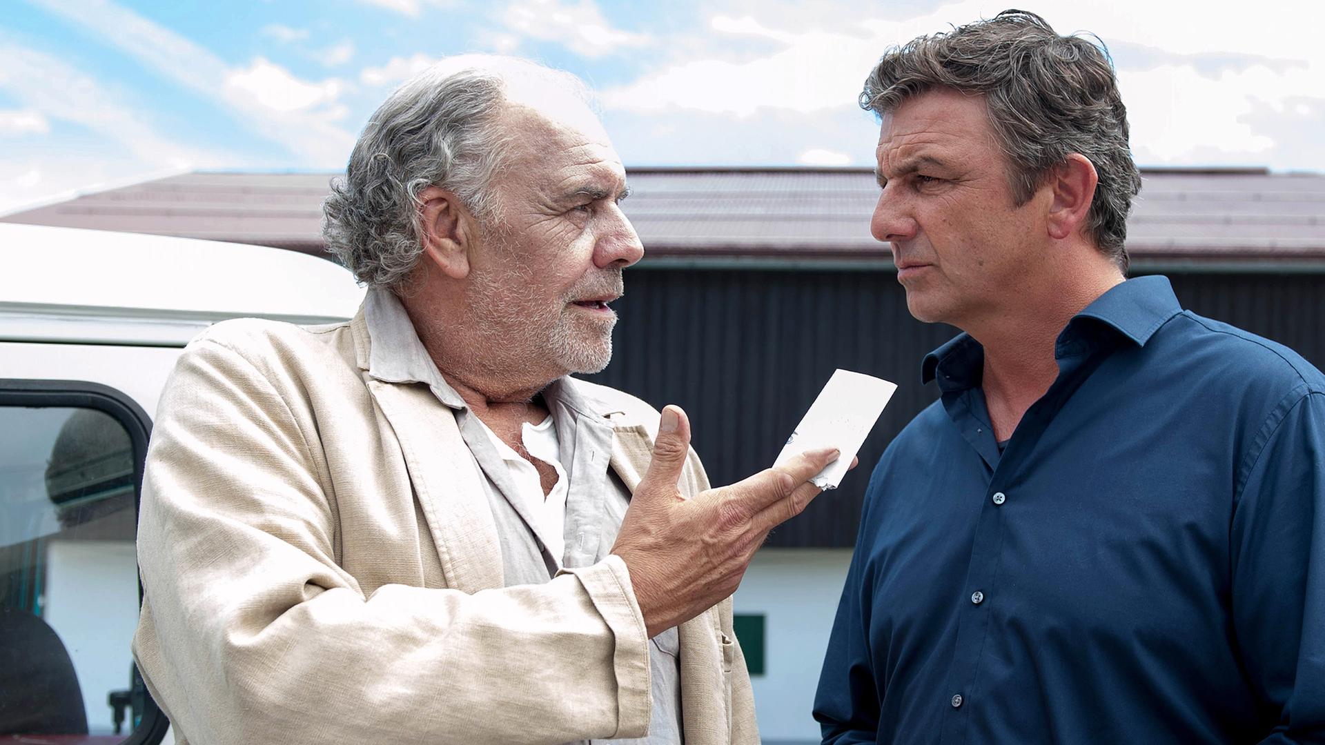 Ludwig (Christian Kohlund), der einen Zettel in der Hand hält, steht neben seinem Neffen Martin Gruber (Hans Sigl) vor dem Haus.