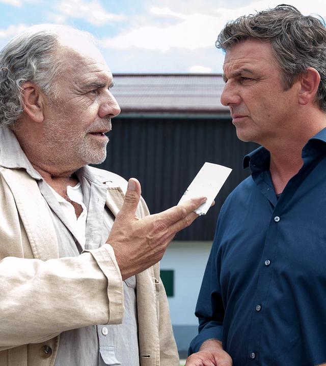 Ludwig (Christian Kohlund), der einen Zettel in der Hand hält, steht neben seinem Neffen Martin Gruber (Hans Sigl) vor dem Haus.