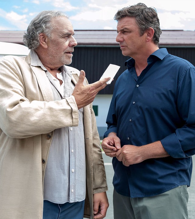 Ludwig (Christian Kohlund), der einen Zettel in der Hand hält, steht neben seinem Neffen Martin Gruber (Hans Sigl) vor dem Haus.