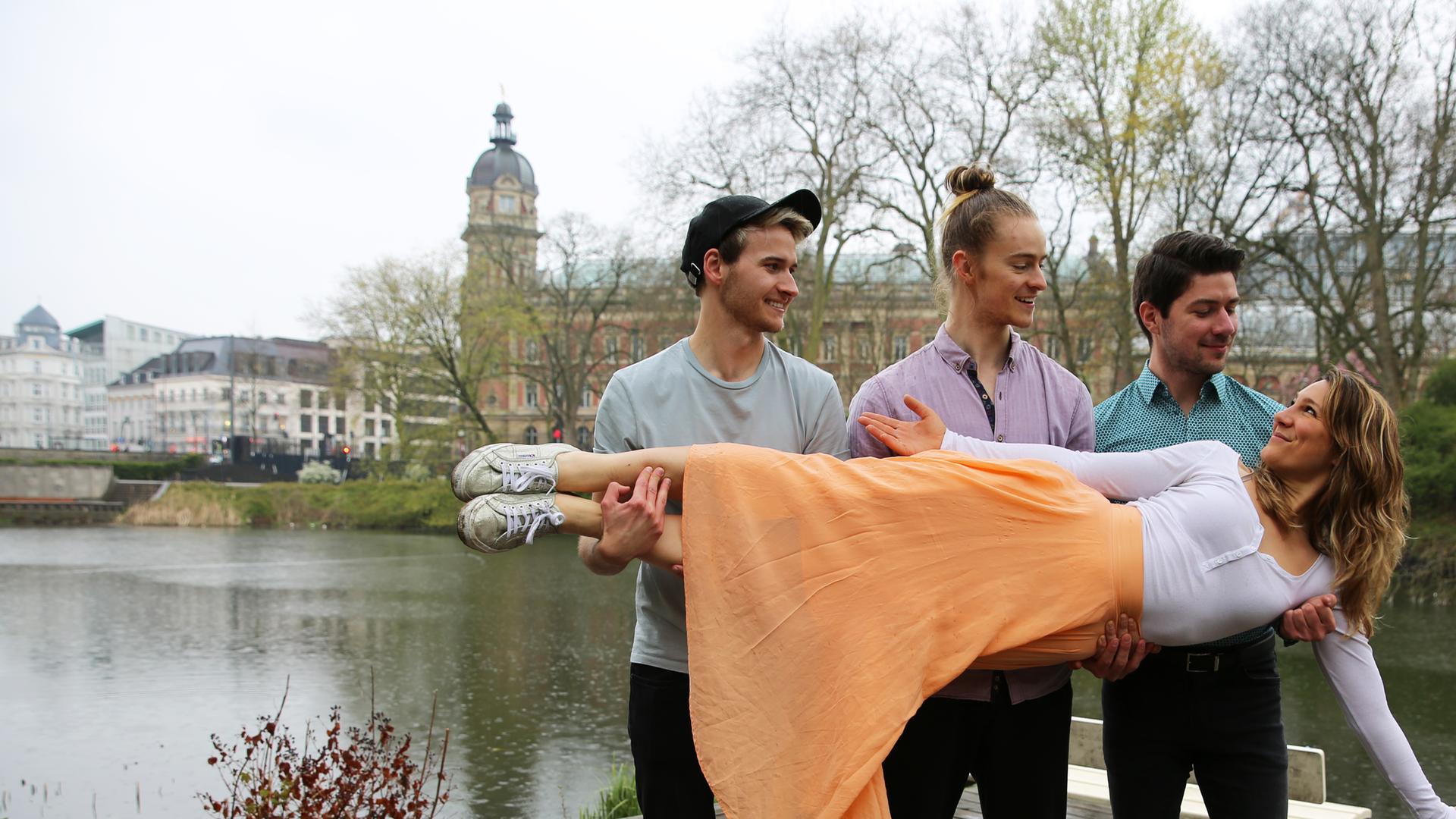 Jasmina Neudecker lässt sich von drei Männern waagerecht auf den Händen tragen und schaut zu ihnen hoch.