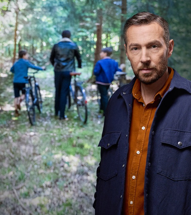 Sven Voss vor einem Foto von 2 Kindern und einem jungen Mann im Wald mit Fahrrädern.