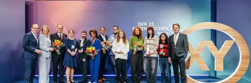 Gruppenfoto Preisträger XY-Preis 2026 mit Alexander Dobrindt, Dr. Nadine Bilke, Dr. Thomas Krull, Dr. Annemarie Krull, Daniel Karstens, Dennenesch Zoudé, Mitri Sirin, Marco Schwarzenberger, Michelle Kuhn, Stella Hinrichs, Valeria Lizenberger, Edanur Karademir, Rudi Cerne 