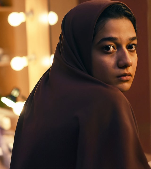  Maryam (Sadaf Asgari) sitzt von einem beleuchteten Schminkspiegel abgewandt.