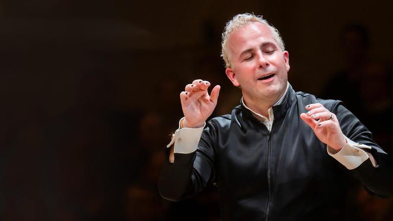 "Neujahrskonzert der Wiener Philharmoniker 2026": Der Dirigent Yannick Nézet-Séguin dirigiert mit beiden erhobenen Armen vor schwarzem Hintergrund. Er dirigiert nur mit den Händen und hat die Augen, wie beseelt, geschlossen.