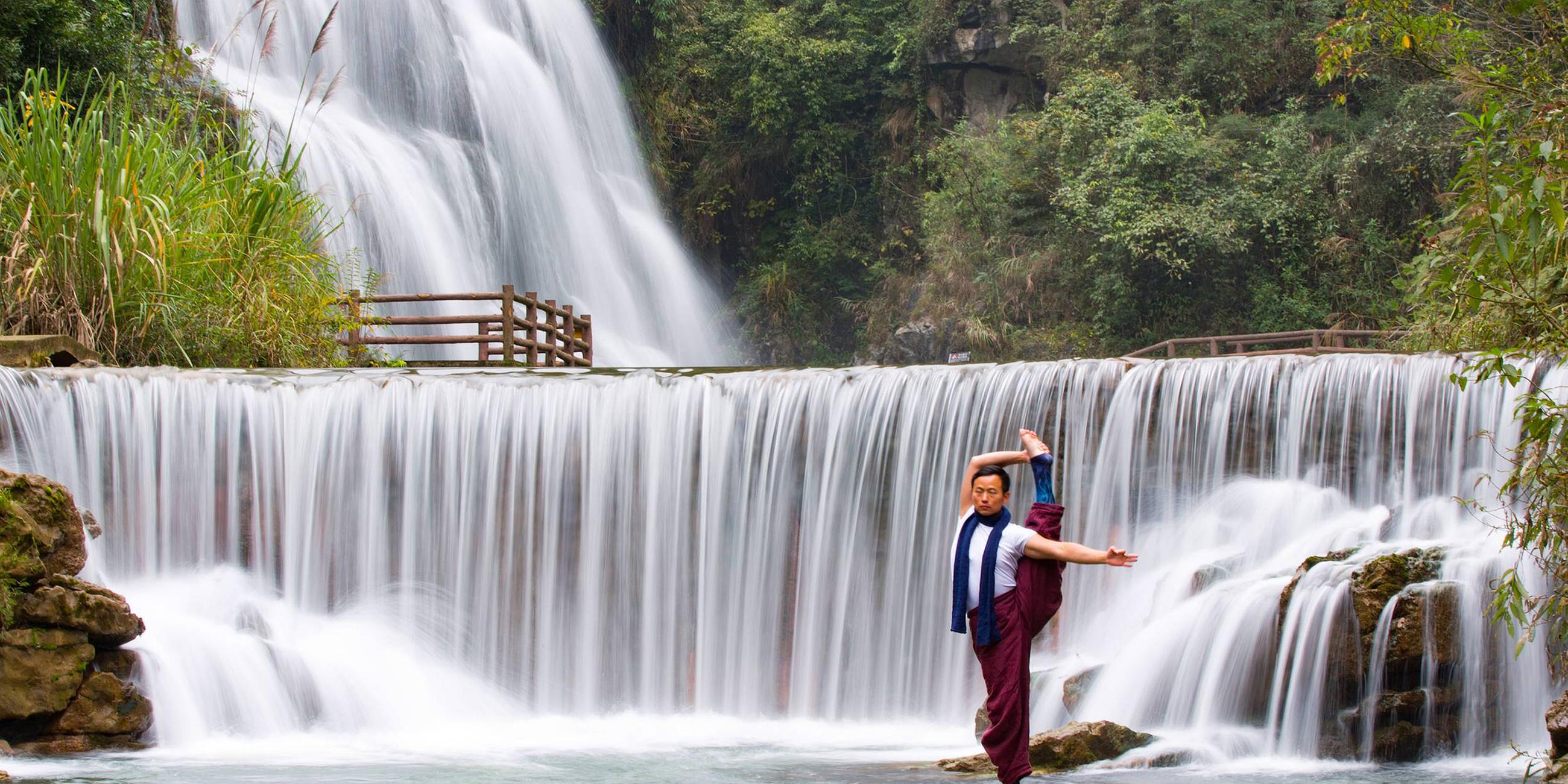 Mann praktiziert Yoga vor einem Wasserfall