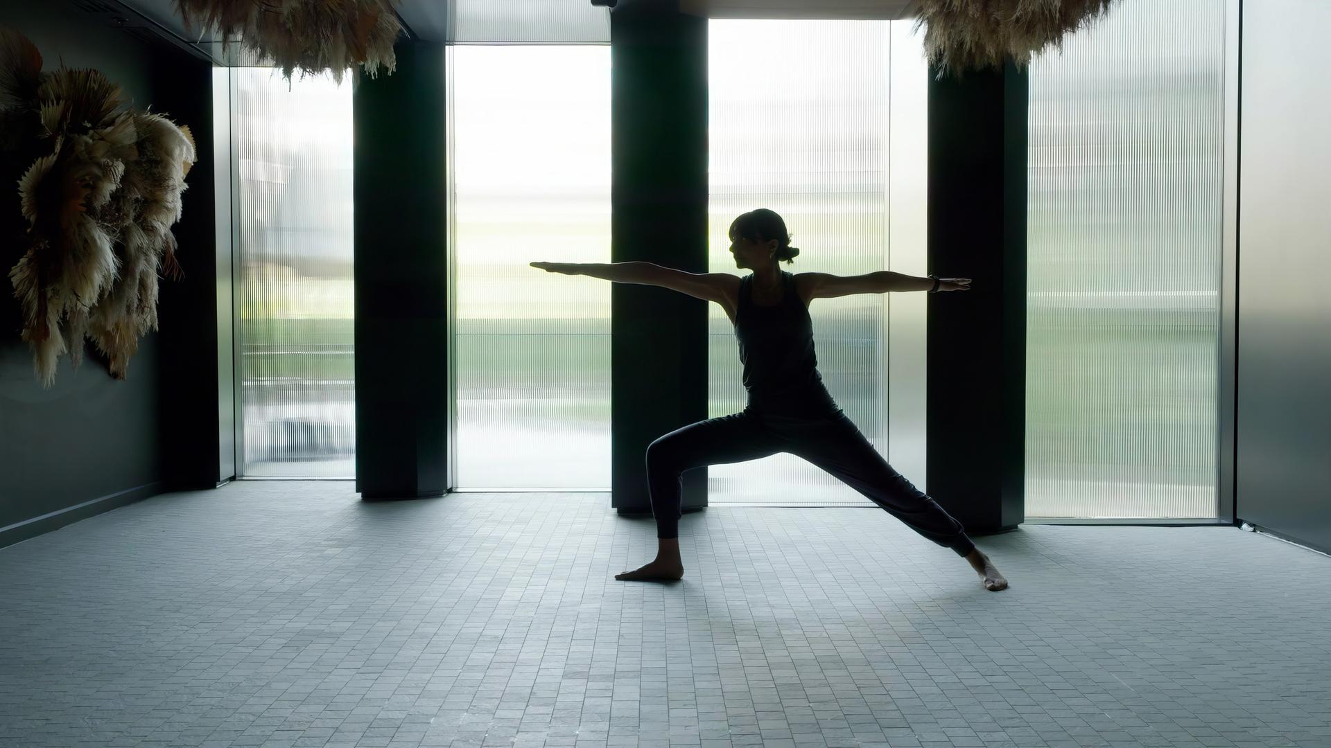 Eine Frau in Yoga-Position als Silhouette vor einem großen Fenster.