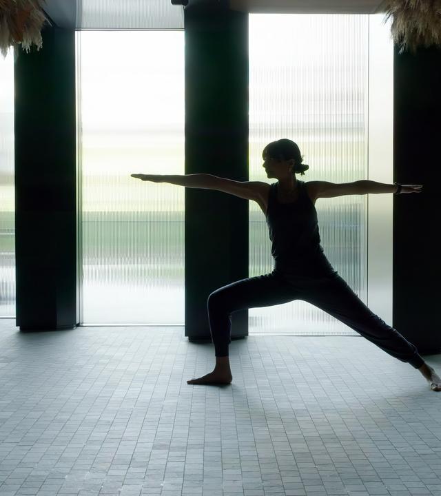 Eine Frau in Yoga-Position als Silhouette vor einem großen Fenster.