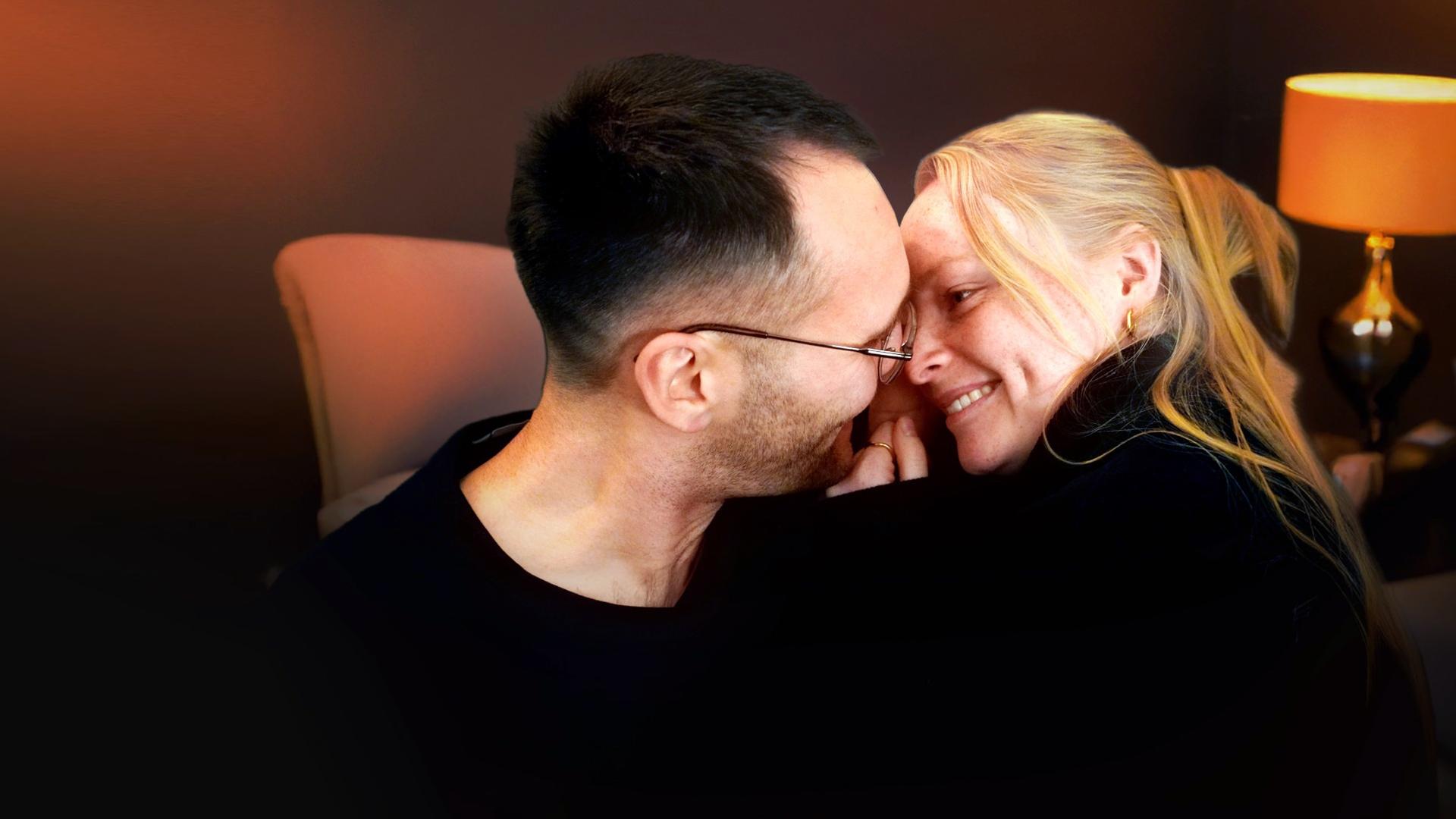 In einem Innenraum: Nico und Josephine schauen sich tief in die Augen und lächeln sich an.