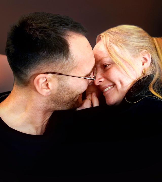 In einem Innenraum: Nico und Josephine schauen sich tief in die Augen und lächeln sich an.