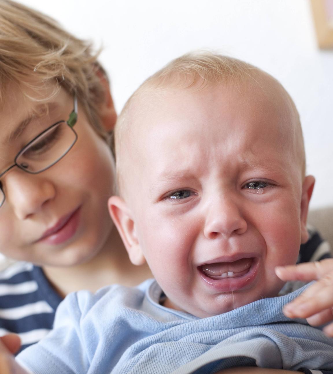 Ein Kleinkind mit zwei kleinen Michzähnen auf dem Arm seines Bruders weint.
