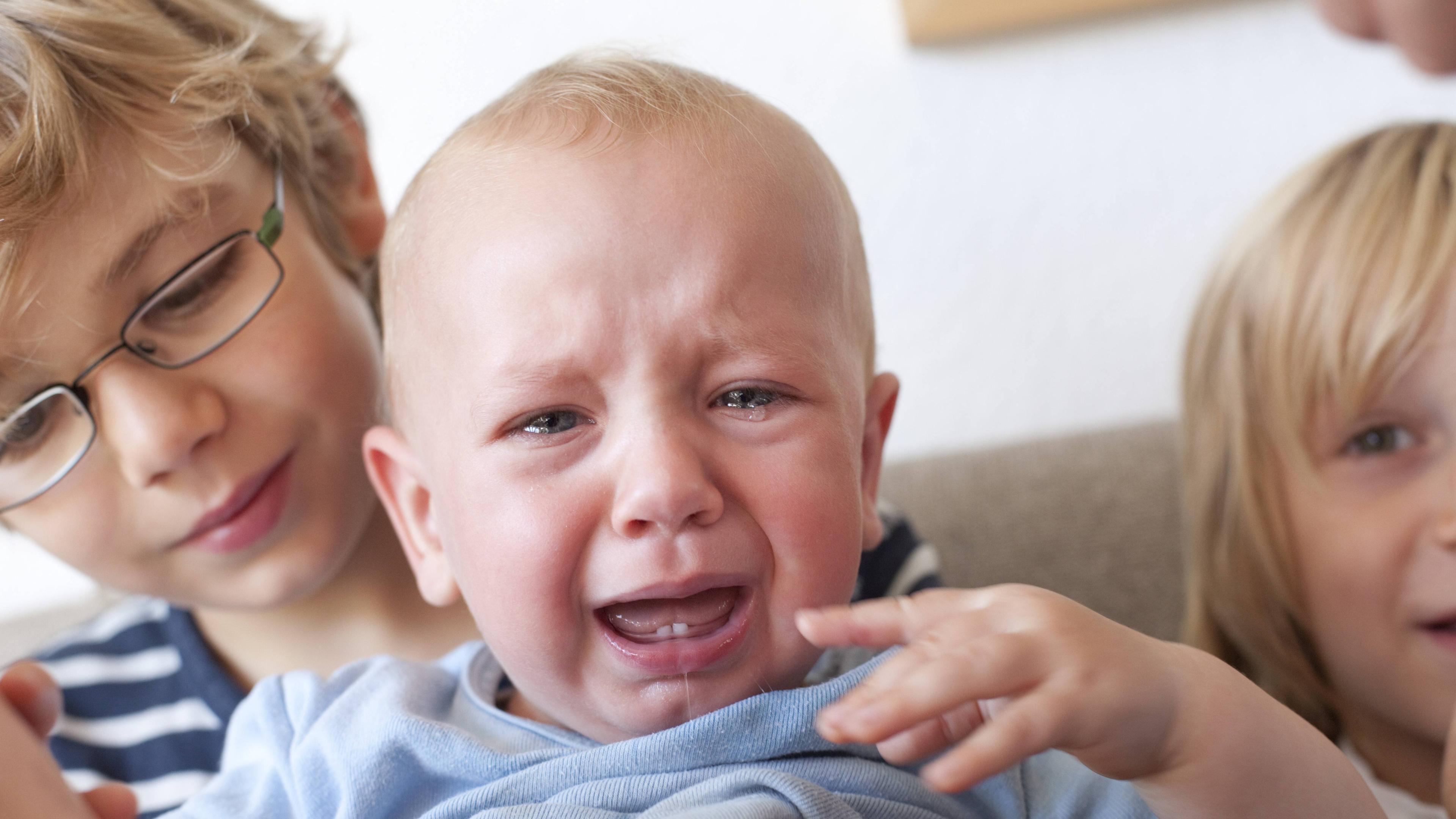 Ein Kleinkind mit zwei kleinen Michzähnen auf dem Arm seines Bruders weint.