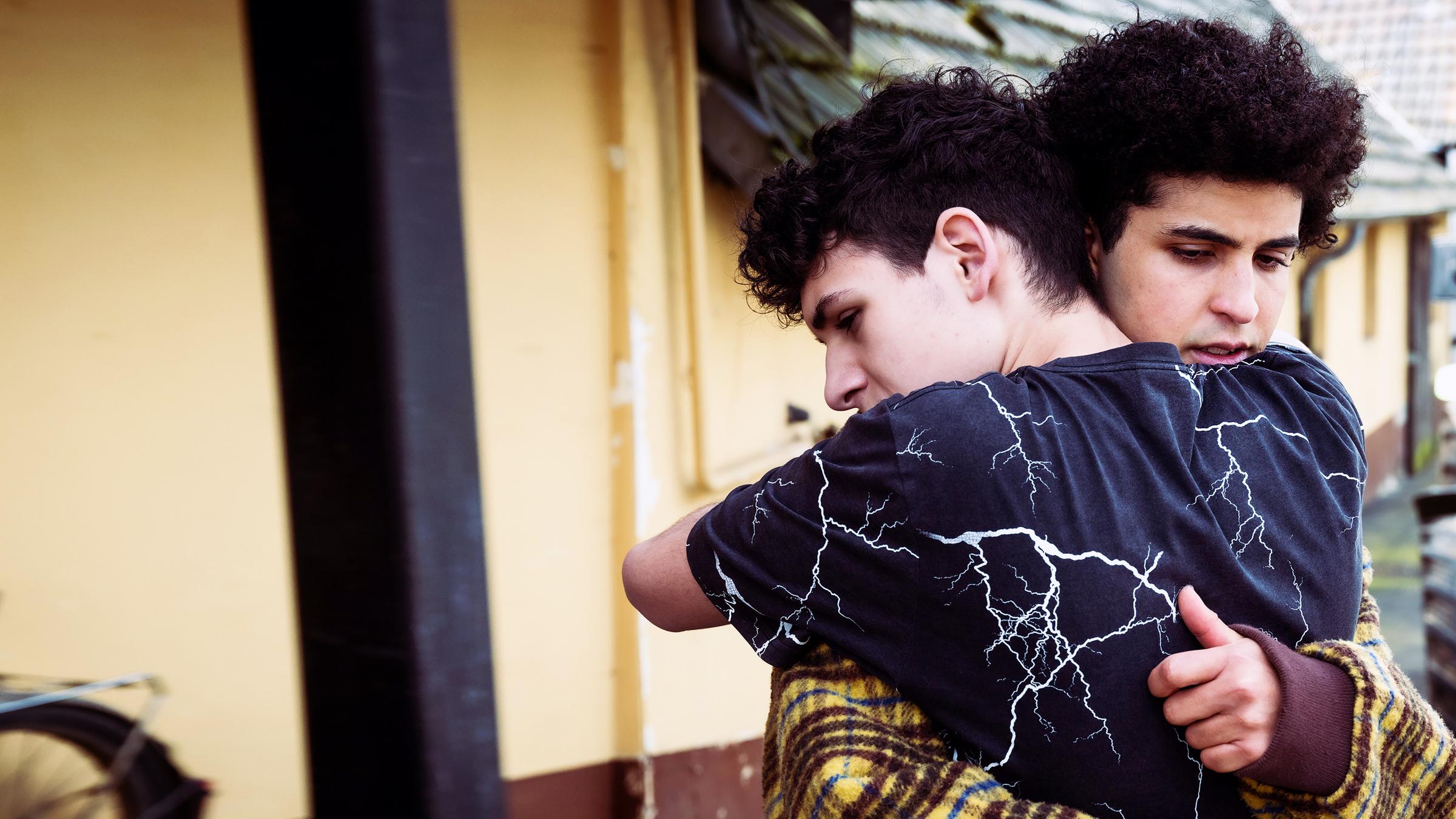 „Von uns wird es keiner sein“: Vor einem Gebäude: Erik (Giuseppe Bonvissuto) umarmt Waldi (Lukas von Horbatschewsky). Im Hintergrund steht ein Traktor.