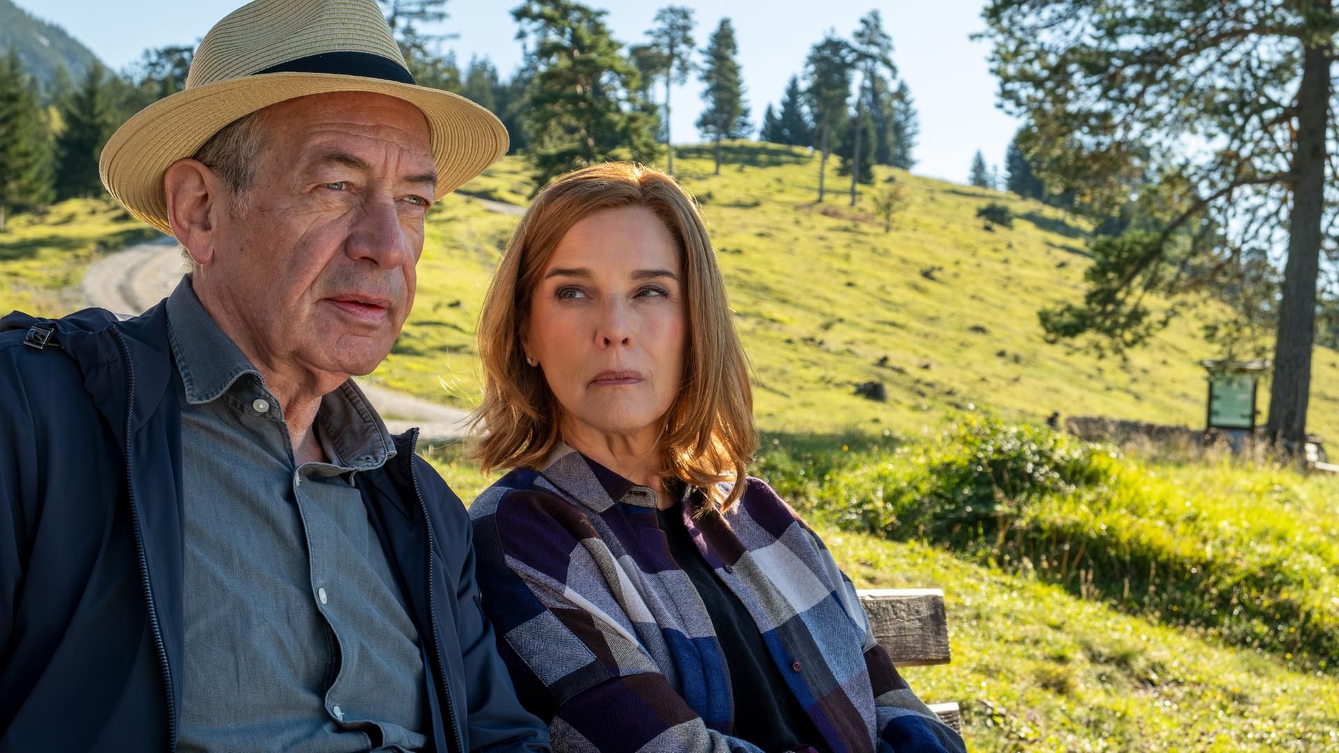 "In fremden Händen": Mit einem Strohhut auf dem Kopf und lässig gekleidet sitzt Witwer Wolfgang (Robert Hunger-Bühler) mit Karola auf einer Bank im Grünen. Karola (Désirée Nosbusch) blickt Wolfgang von der Seite aus kritisch an. Die Schultern des Paares berühren 