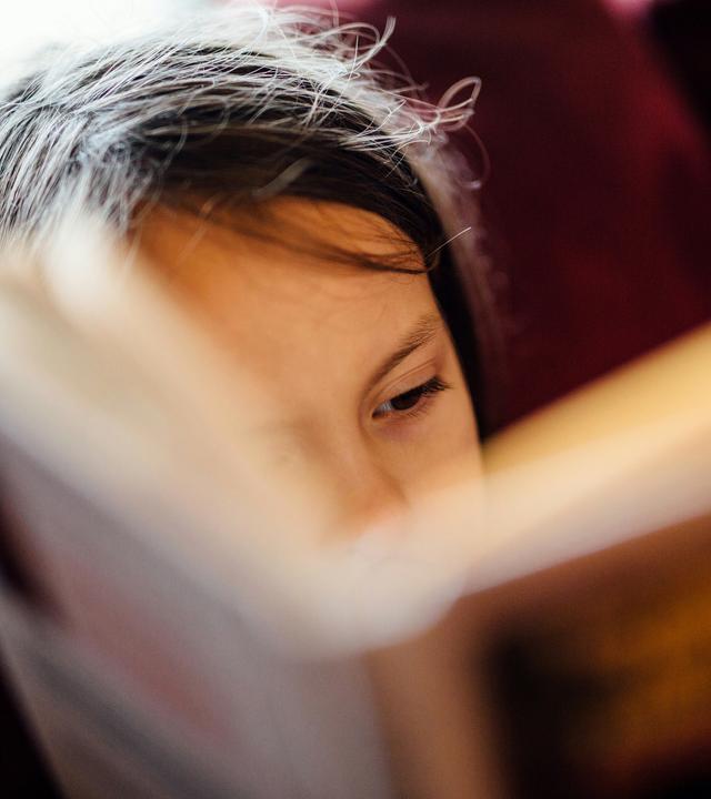 Nahaufnahme: ein Mädchen liest in einem Buch, das im Vordergrund unscharf ist