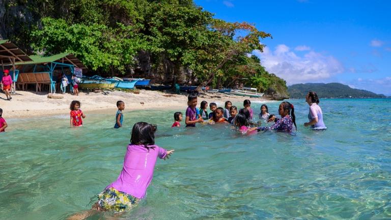 Kinderhilfe Philippinen: Eine Gruppe von Kindern und ihre Betreuerin baden im seichten Wasser am Strand