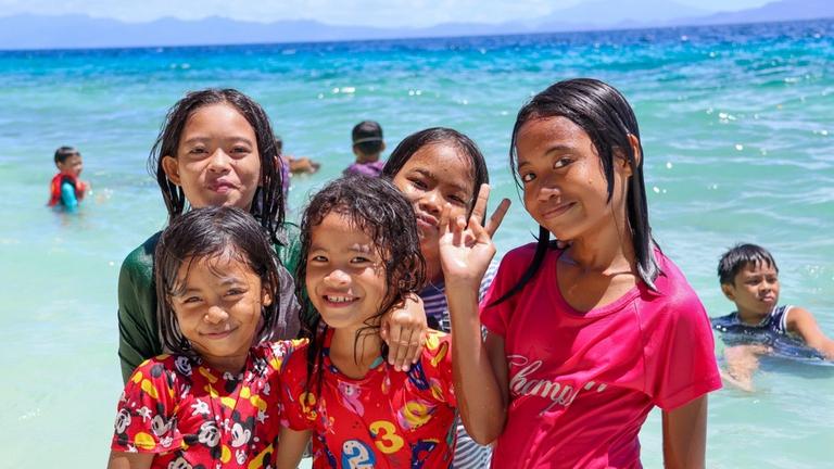 Kinderhilfe Philippinen: Fünf Mädchen stehen am Strand im seichten Wasser und lächeln in die Kamera