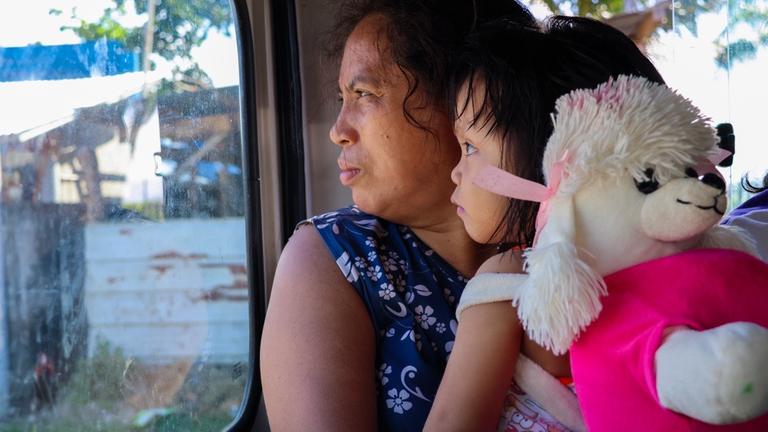 Kinderhilfe Philippinen: Eine Frau hält ein kleines Mädchen im Arm, das einen Rucksack in Form eines Pudels trägt