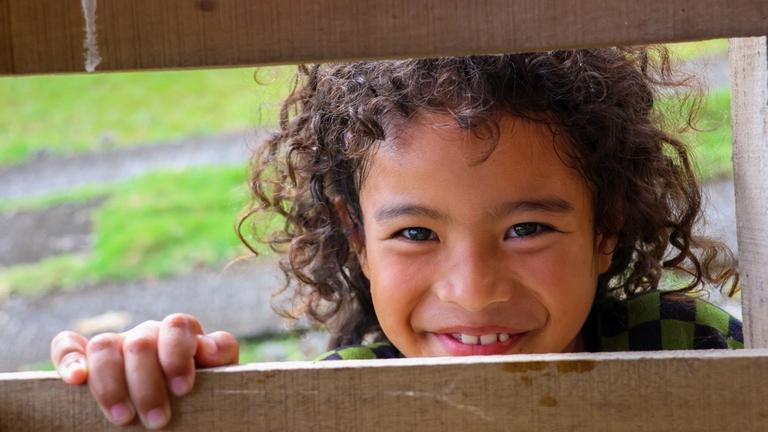 Kinderhilfe Philippinen: Ein kleines Mädchen schaut lächelnd durch einen Bretterzaun
