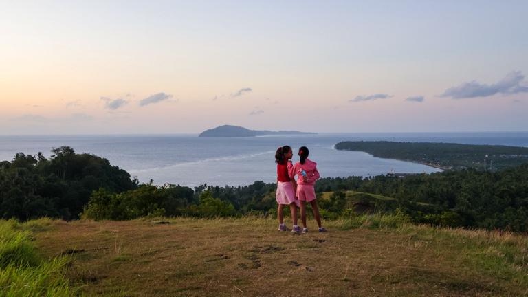 Kinderhilfe Philippinen: Zwei junge Frauen stehen auf einer Anhöhe. Im Hintergrund Sonnenaufgang über dem Meer