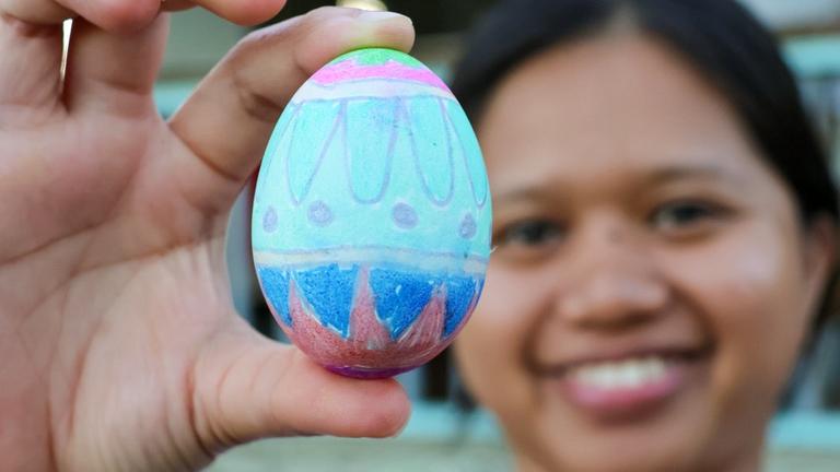 Kinderhilfe Phlippinen: Ein Mädchen hält ein bemaltes Osterei in die Kamera und lächelt