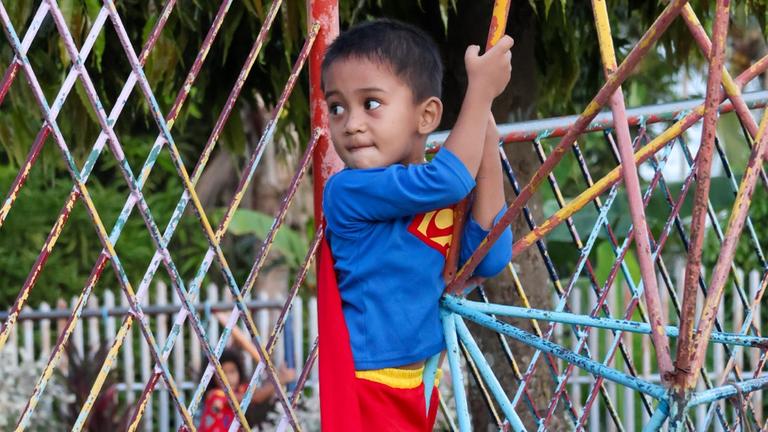 Kinderhilfe Philippinen: Ein kleiner Junge im Superman-Kostüm steht auf einem Klettergerüst