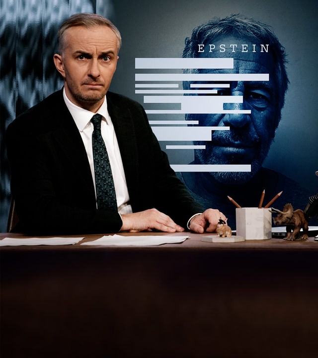 Jan Böhmermann sitzt mit ernster Miene am Schreibtisch. Rechts im Hintergrund ist das Portrait von Jeffrey Epstein.