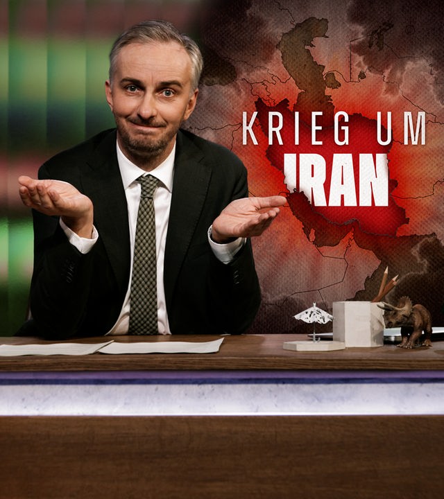 Jan Böhmermann sitzt mit ernster Miene am Schreibtisch. Rechts im Hintergrund eine Landkarte mit Schriftzug "Krieg um Iran".
