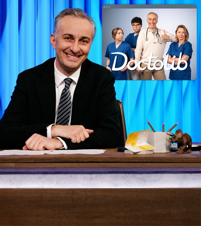 Jan Böhmermann sitzt lachend am Schreibtisch. Rechts im Hintergrund ist ein Arzt und drei Krankenschwestern zu sehen