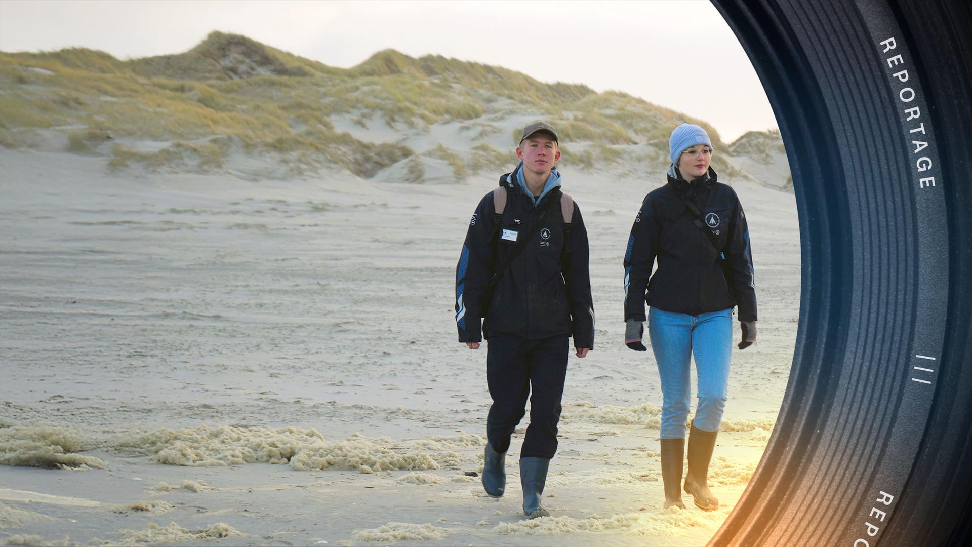 Strand auf Amrum. Im Vordergrund rechts eine junge Frau mit blauer Wollmütze, links ein junger Mann. Beide tragen eine schwarze Jacke.