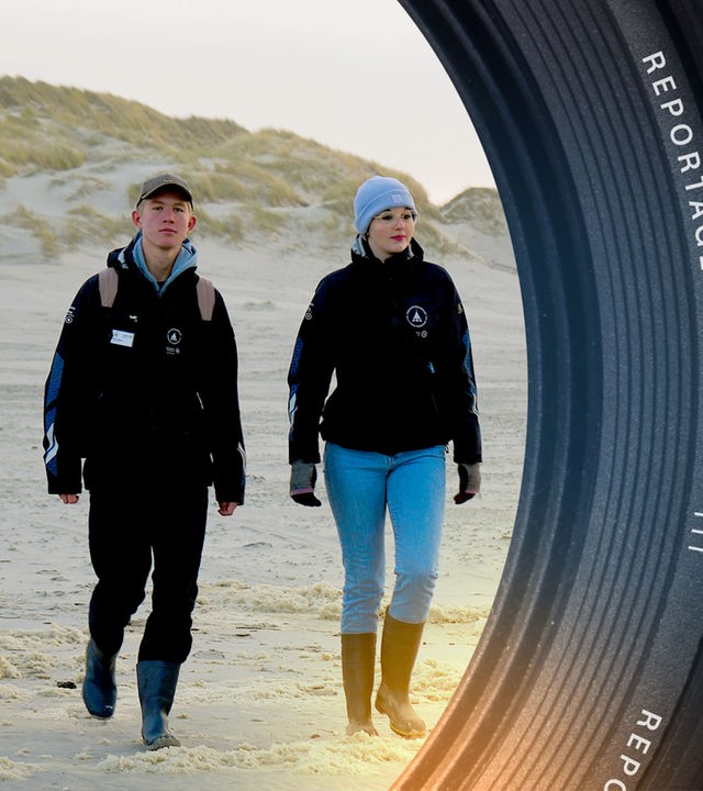 Strand auf Amrum. Im Vordergrund rechts eine junge Frau mit blauer Wollmütze, links ein junger Mann. Beide tragen eine schwarze Jacke.