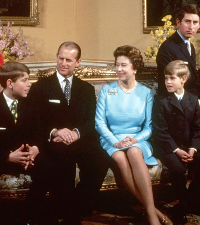 Die britische Königsfamilie rund um Queen Elizabeth II. ist auf dem Bild zu sehen. Charles und Anne auf den Armlehnen der Couch, Andrew und Edward neben ihren Eltern Philip und Elizabeth.