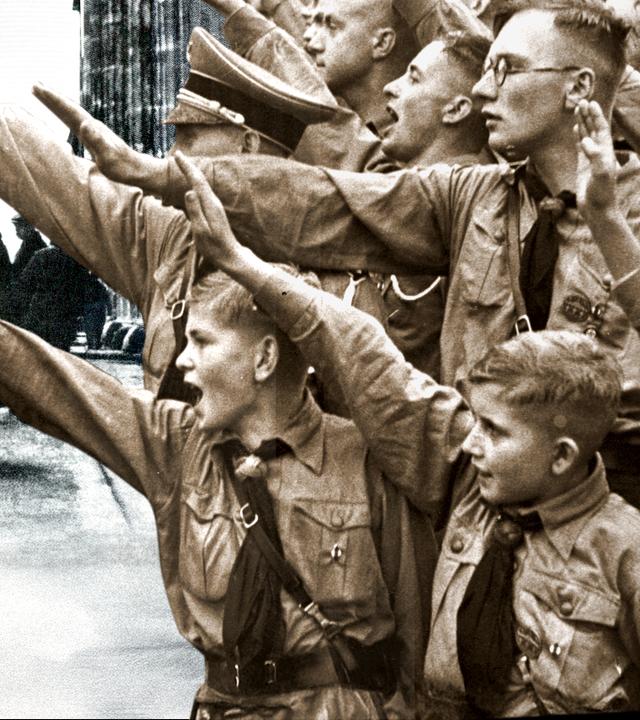Junge Nationalsozialisten machen den Hitlergruß, im Hintergrund der brennende Reichstag.