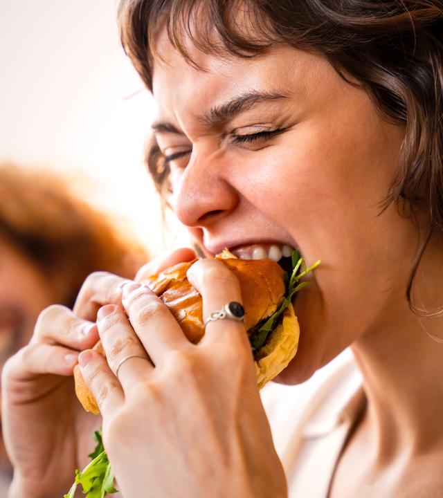 Nahaufnahme, eine junge Frau beißt leidenschaftlich in einen großen Burger.